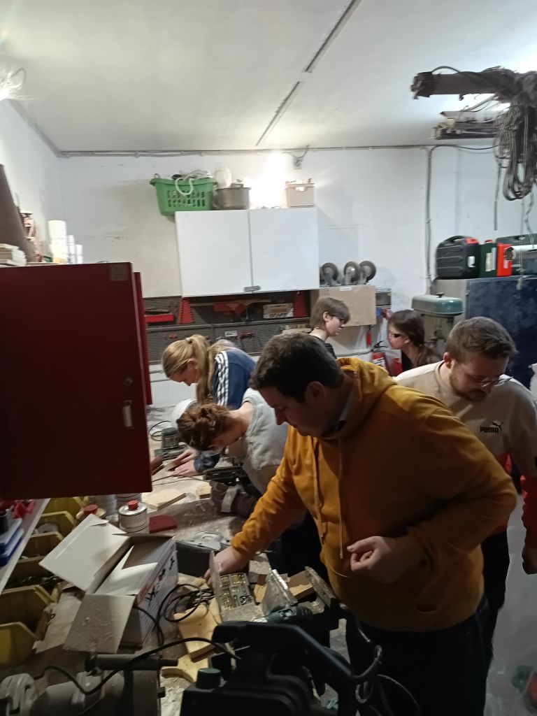 Mehrere Frauen und Männer arbeiten mit Werkzeugen an einer Werkbank.