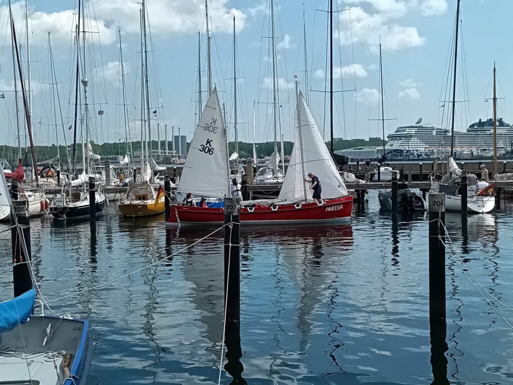 Rotes Segelboot mit zwei Masten fährt durch einen Hafen.